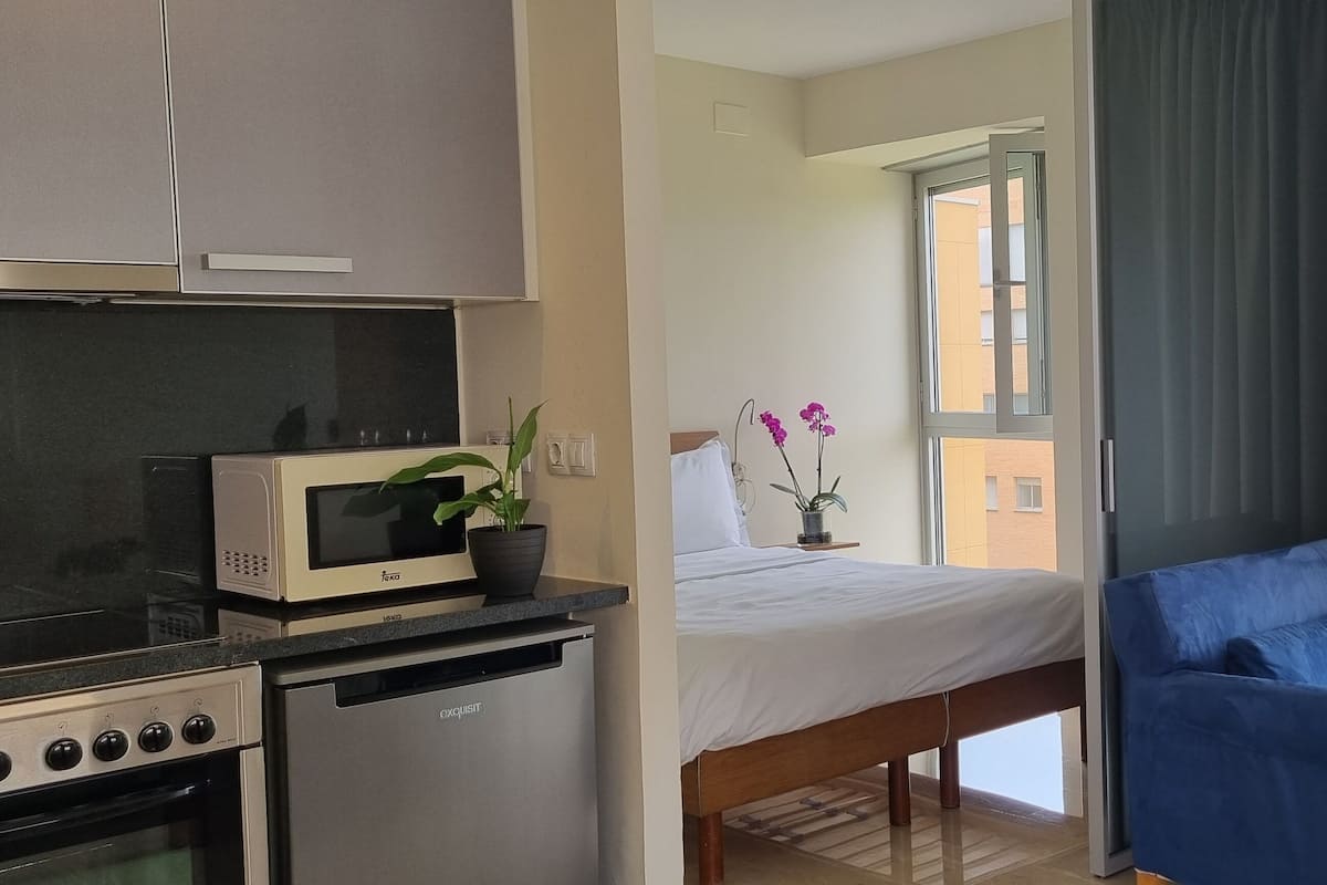Un dormitorio con cama, sofá azul, microondas, horno y una planta en maceta.