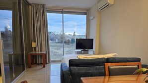 Habitación de hotel con balcón, cama, televisor, sofá y mesa.