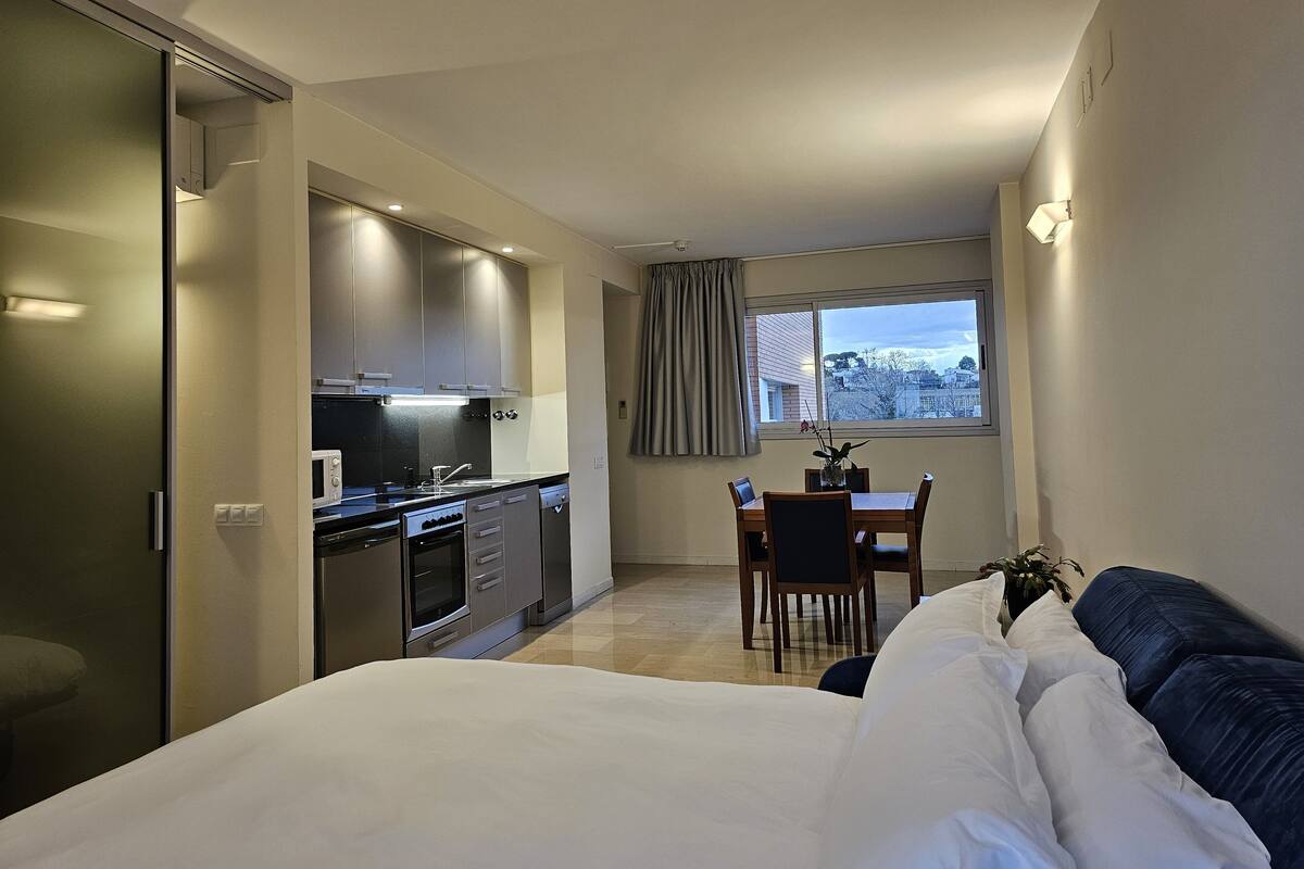 Una habitación de hotel moderna con kitchenette, comedor y una cama grande.