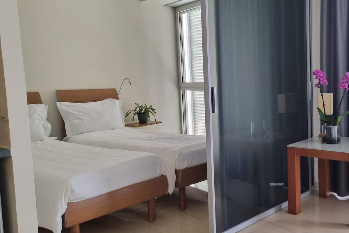 Habitación de hotel con dos camas, una mesita con un florero, una cafetera y un puerta corredera.