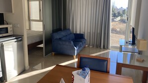 Una habitación de hotel moderna con sofá, una mesa de comedor, una botella de agua, microondas y refrigerador.