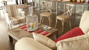 A modern living room with a wooden coffee table, striped armchairs, and a red cushion. A birdcage with a yellow bird is on the table. - Le Château des Magnans (Jausiers)