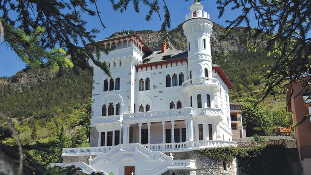 A large, white building with multiple windows and a tower, surrounded by greenery and hills. - Le Château des Magnans (Jausiers)