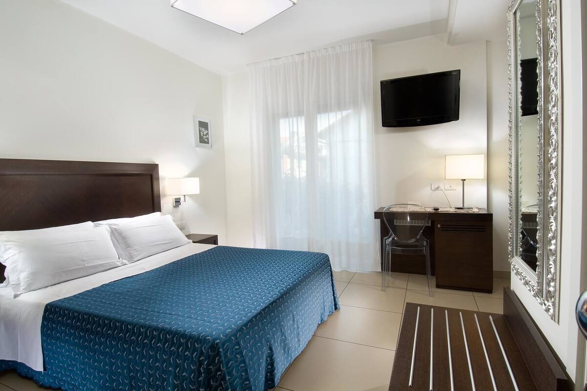A hotel room with a bed, a desk, a chair, a television, and a large mirror.