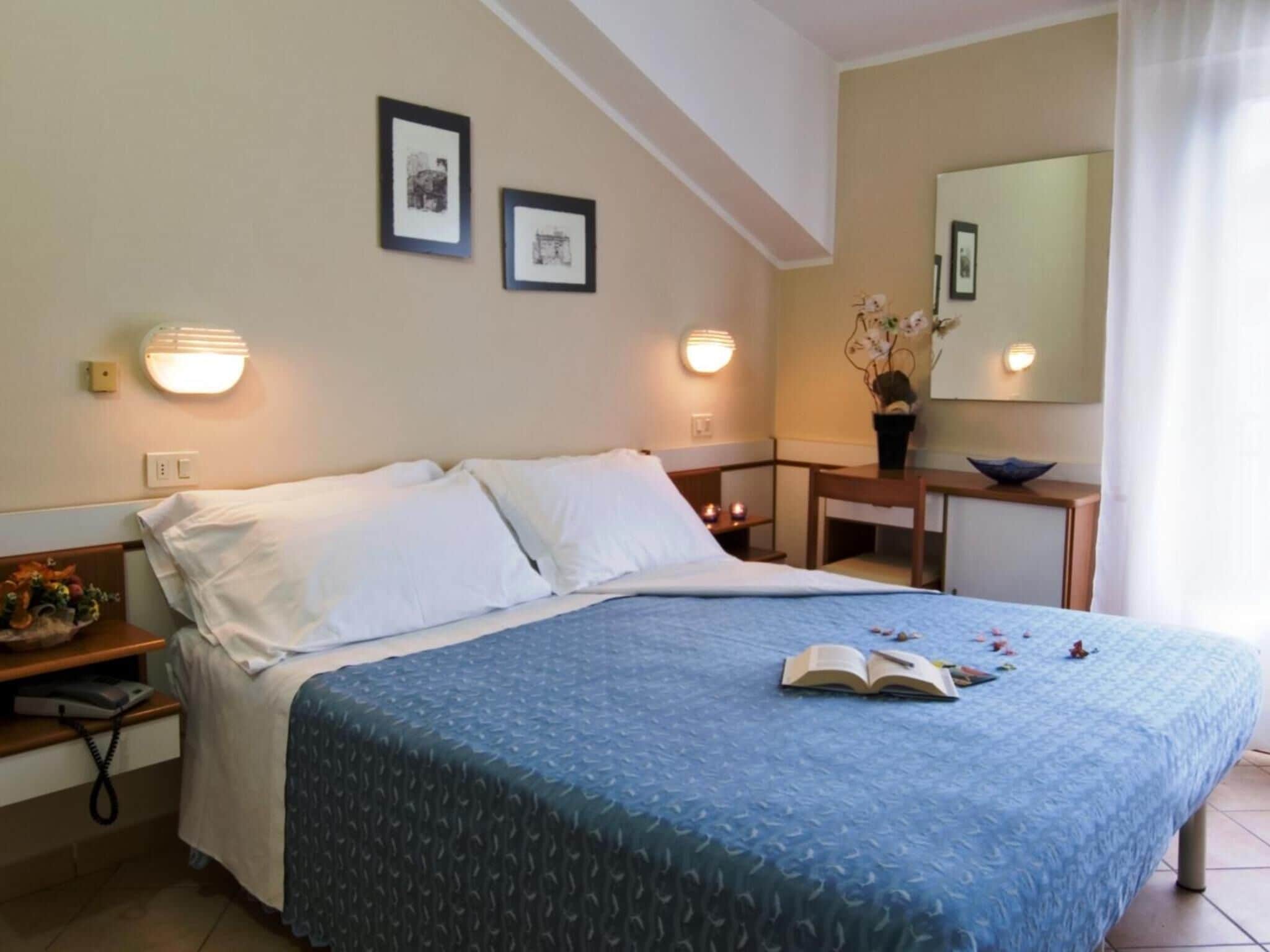 Ein Hotelzimmer mit Bett, Nachttisch, Lampe und Wandbildern.