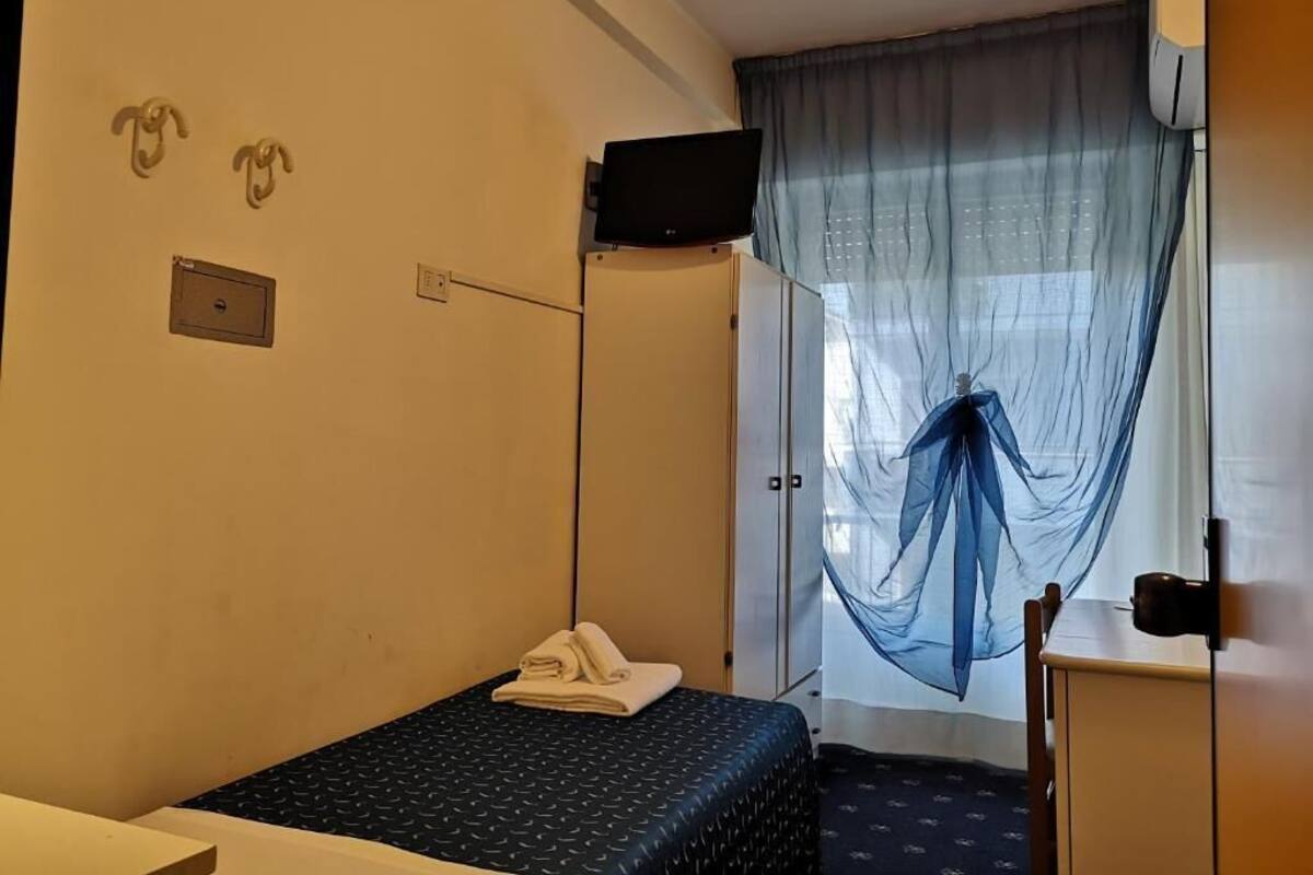 A small, simple room with a bed, a desk, and a TV.