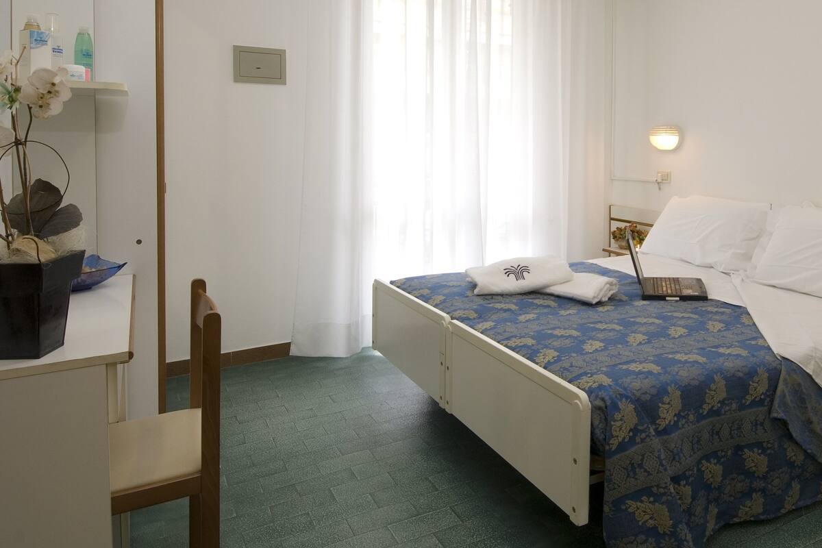 A hotel room with a bed, bedside table, lamp, and a small shelf with toiletries.
