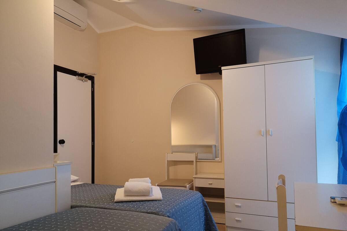 A hotel room with two beds, a wardrobe, a desk, and a TV mounted on the wall.