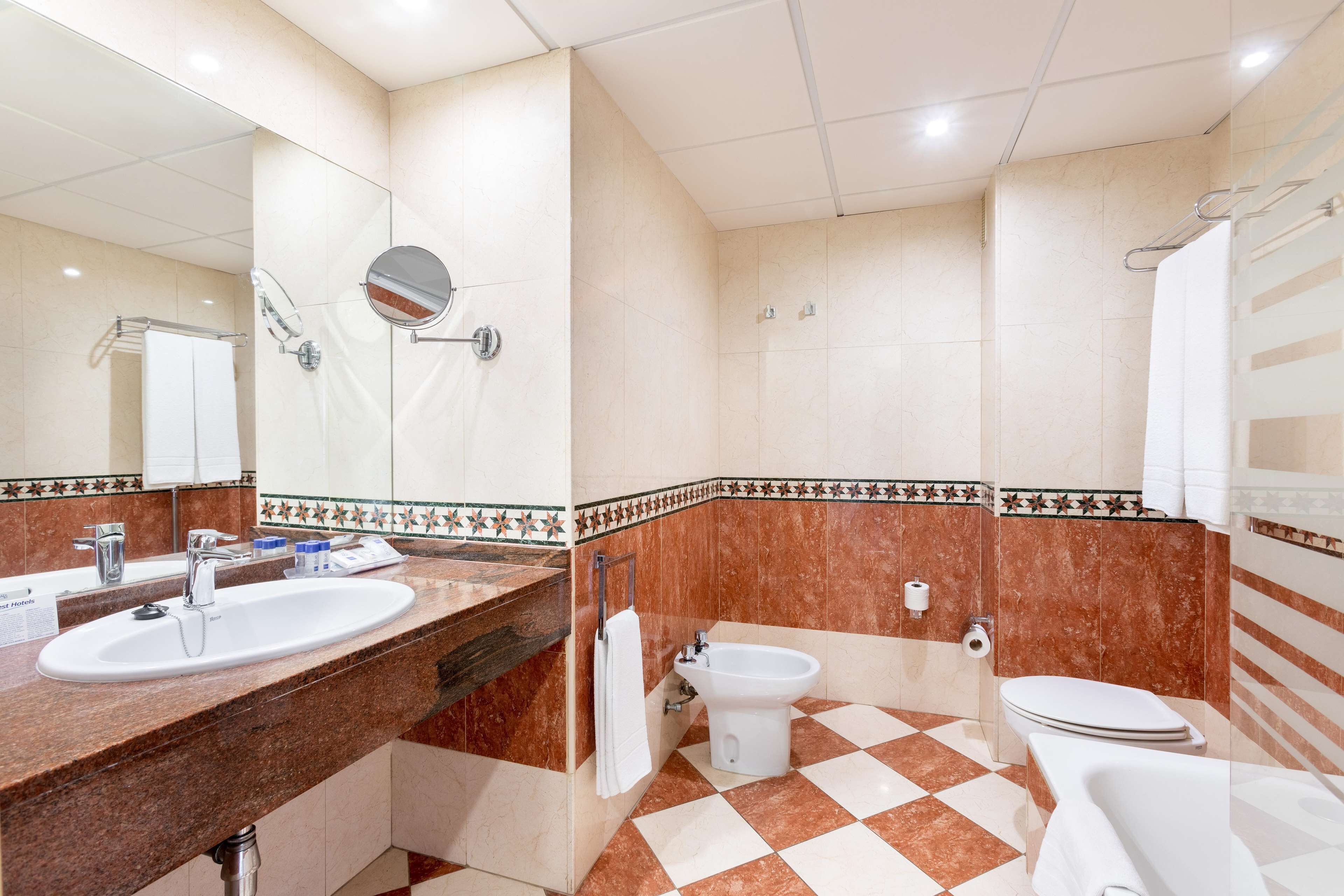 A bathroom with a sink, mirror, bidet, toilet, and shower.