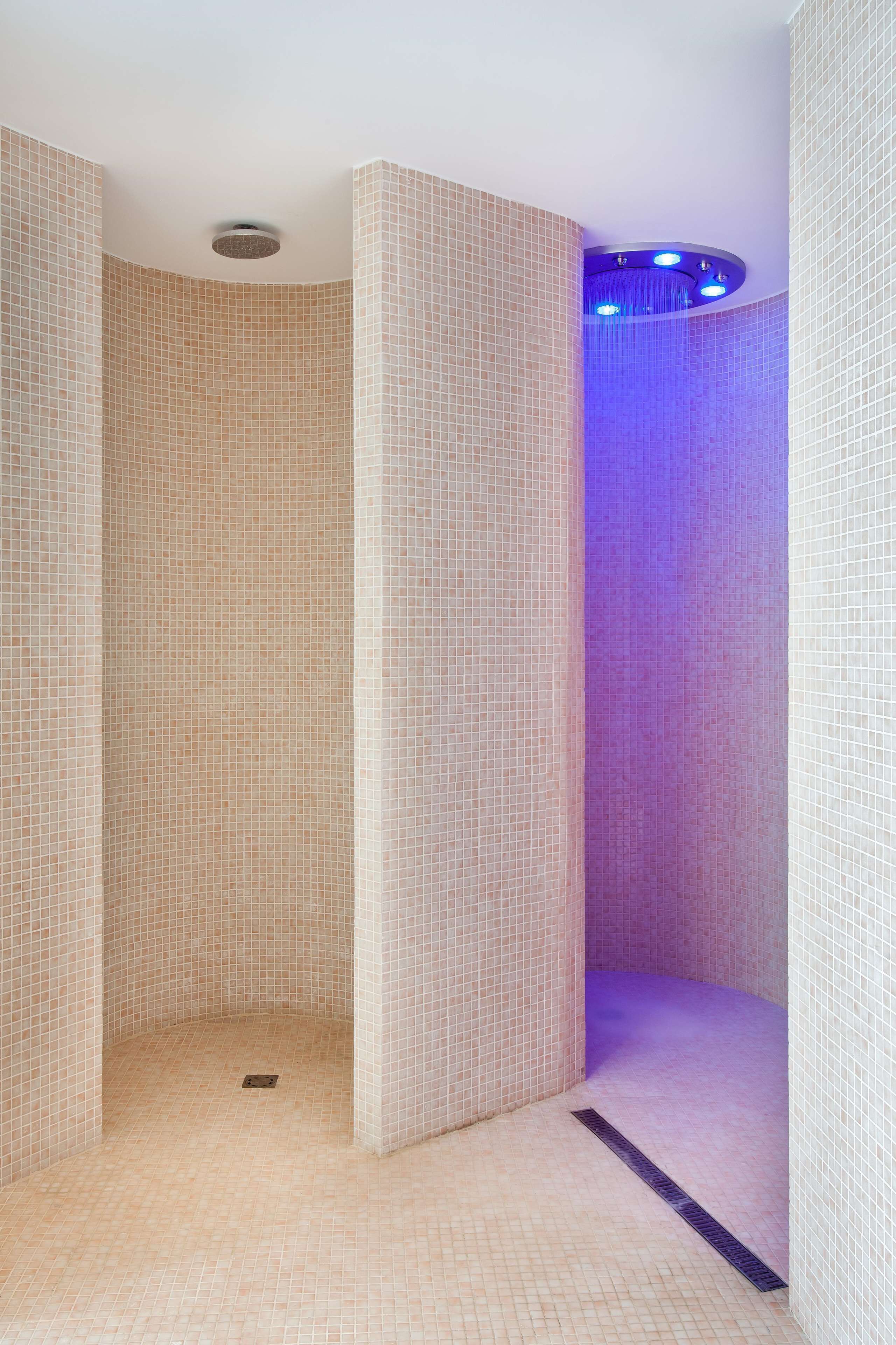 A tiled shower area with a drain and a blue light fixture.