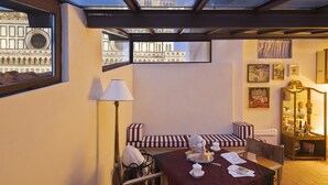 A cozy room with a table set for tea, a sofa, and a lamp. A window reveals a building with intricate architecture. - Granduomo Charming Accomodation (Florence)