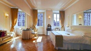 A hotel room with a bed, a sofa, a dining table, and a chair. There are windows with curtains and a painting on the wall. - Granduomo Charming Accomodation (Florence)