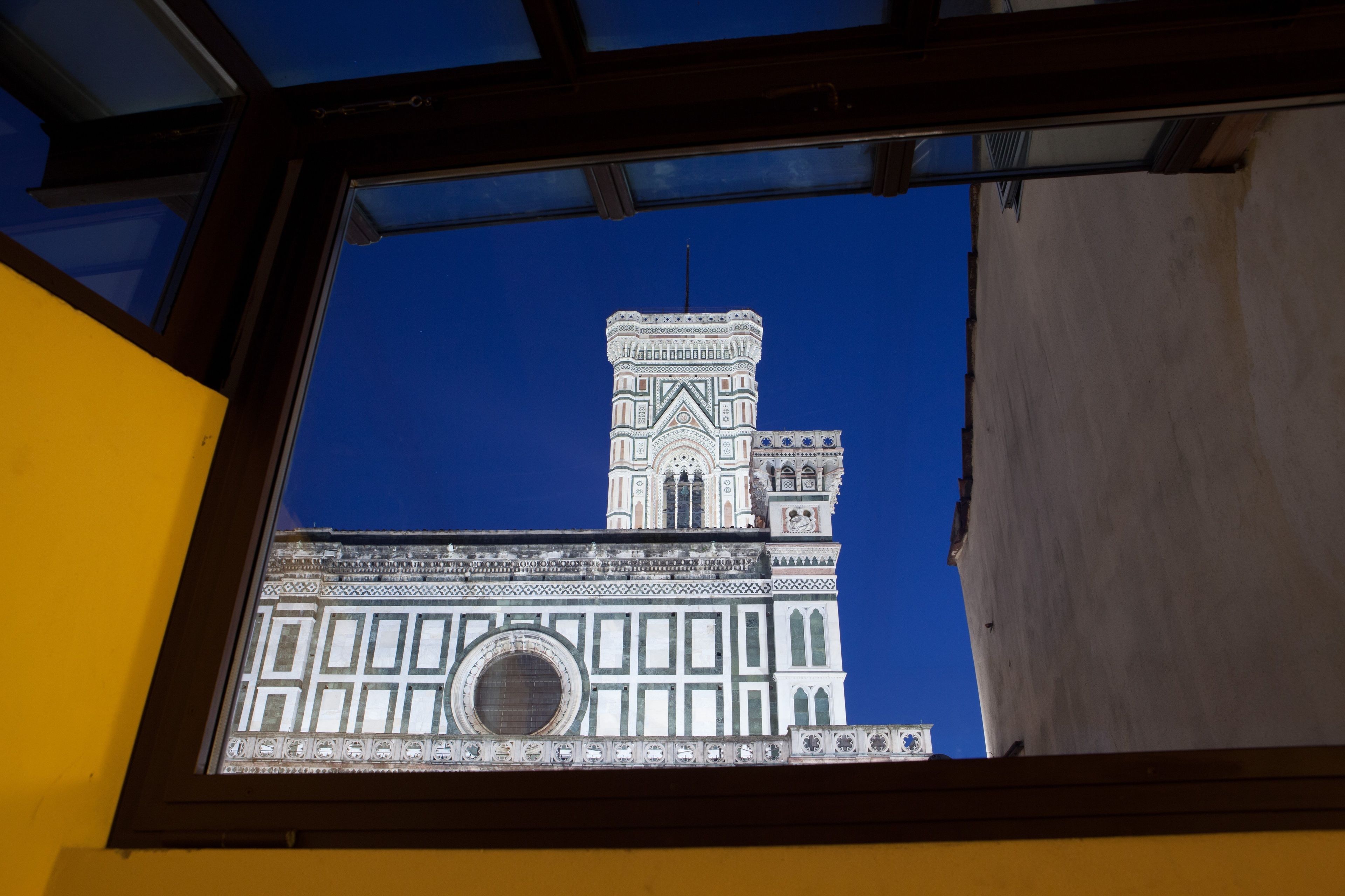 A view of a building's facade through a window, featuring a prominent tower with detailed architectural patterns and a large circular window.