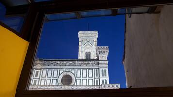 A view of a building's facade through a window, featuring a prominent tower with detailed architectural patterns and a large circular window.
