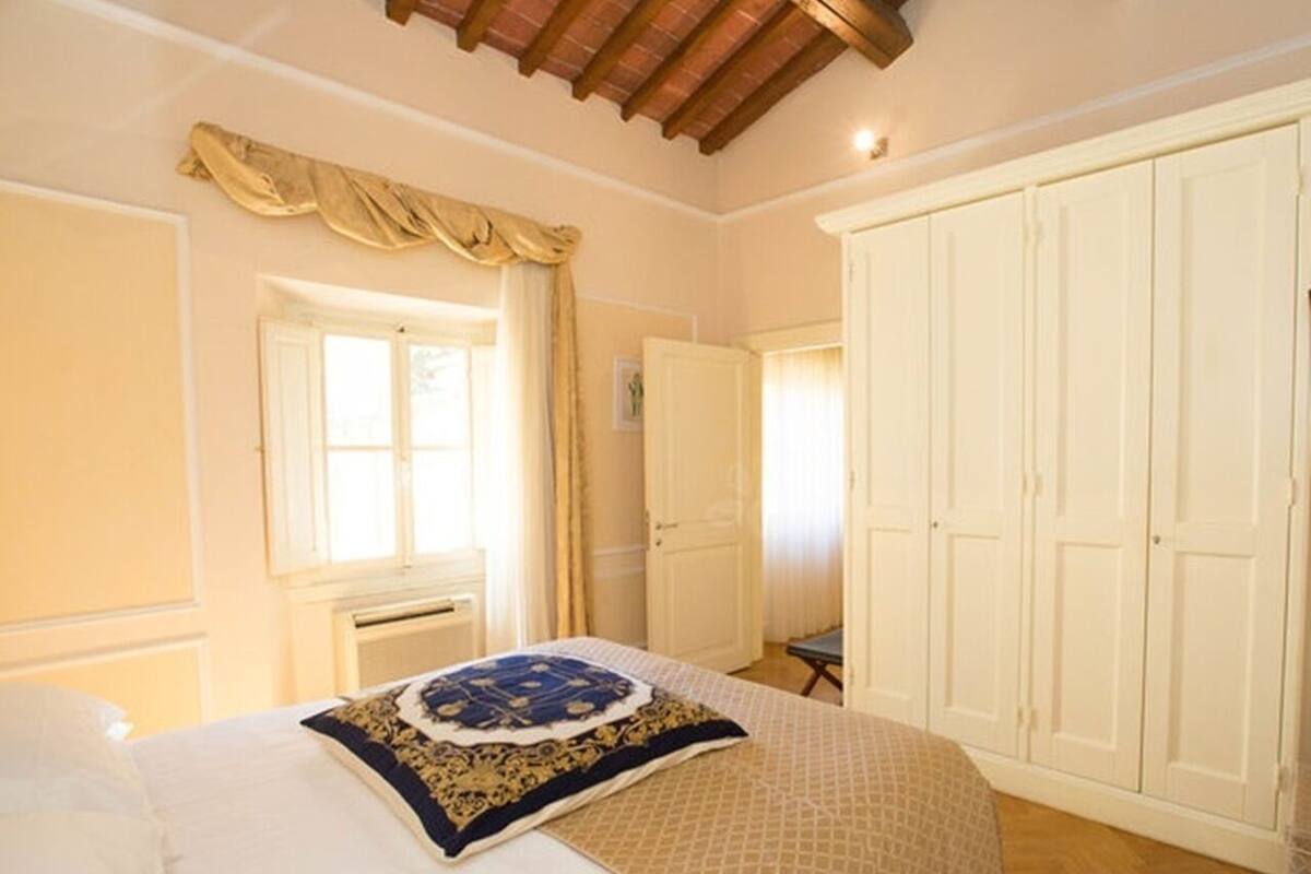 Un dormitorio con cama, ventana con cortinas, armario y techo con vigas de madera.