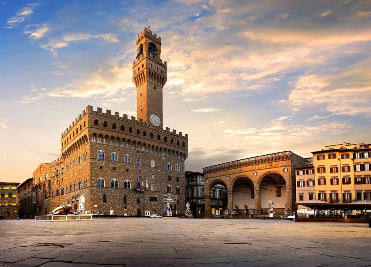 A historic building with a prominent clock tower, a large open plaza, and classical architecture.