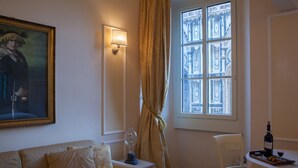 A room with a sofa, a table with a bottle and glasses, a lamp, and a window with curtains. - Granduomo Charming Accomodation (Florence)