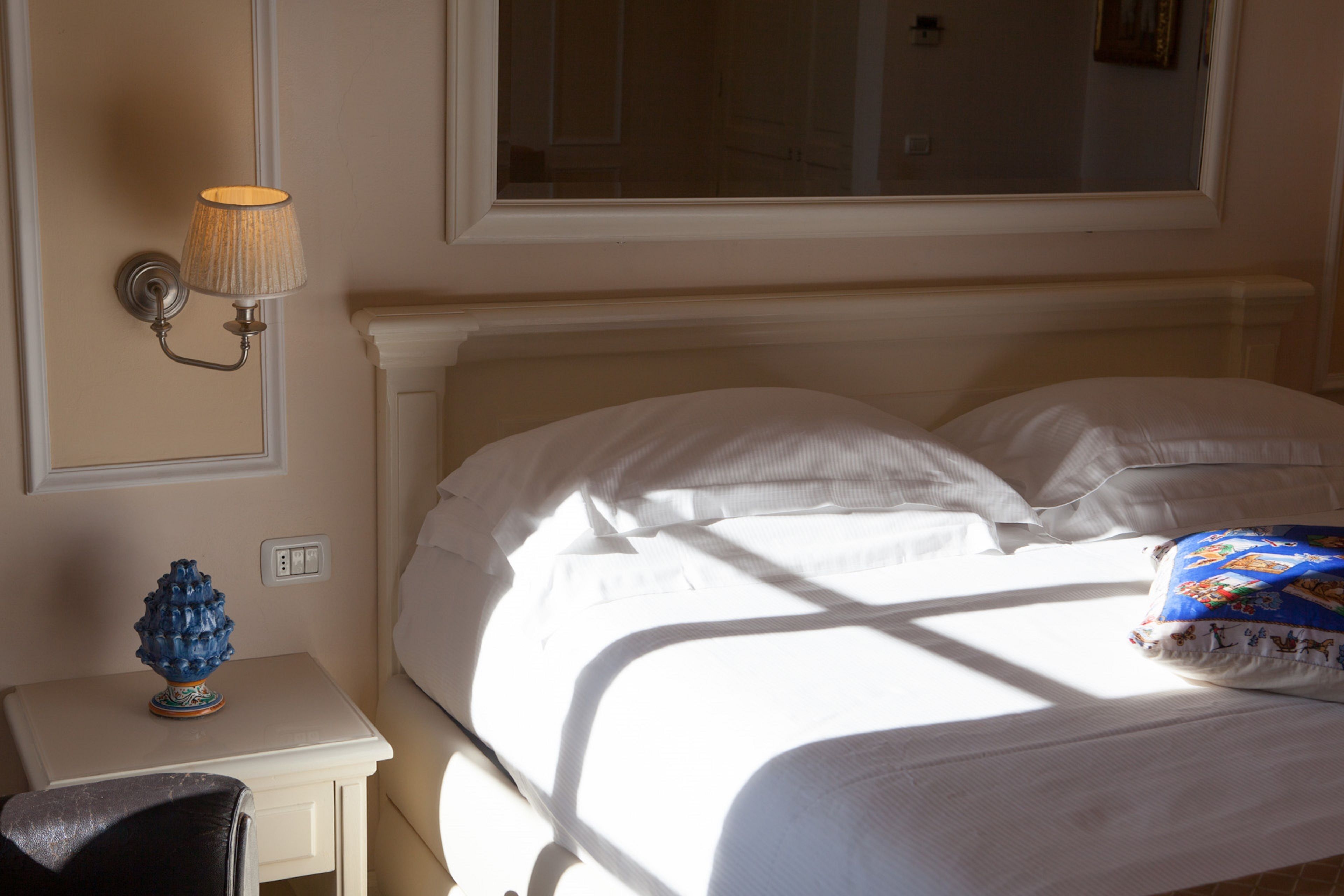 Un lit bien fait, avec du linge de lit blanc, une lampe sur une table de chevet et une fenêtre au-dessus du lit.