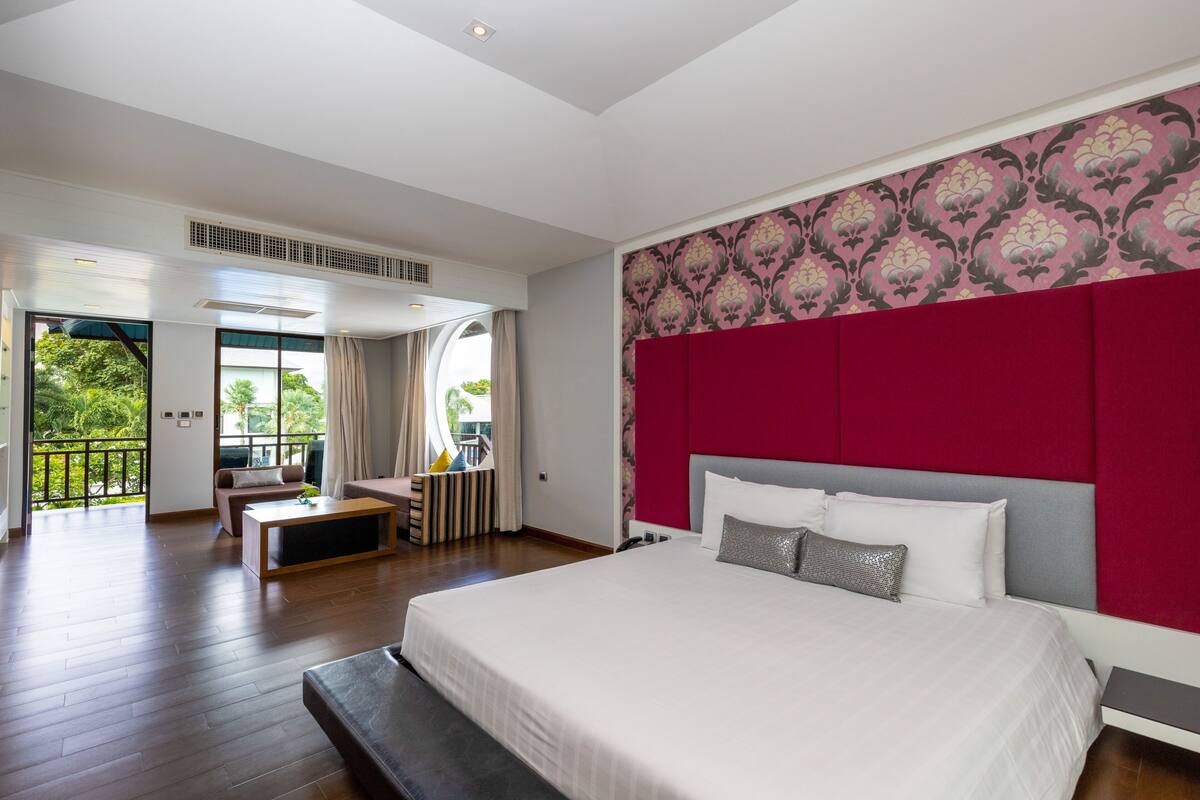 Quarto moderno com uma cama grande, uma parede de destaque vermelha e vista para o exterior.