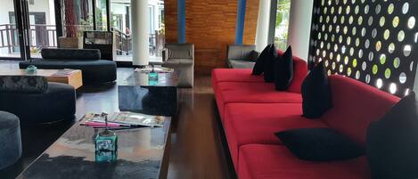 A modern lounge area with a red sofa, black and red cushions, and a glass coffee table with magazines and a water bottle.
