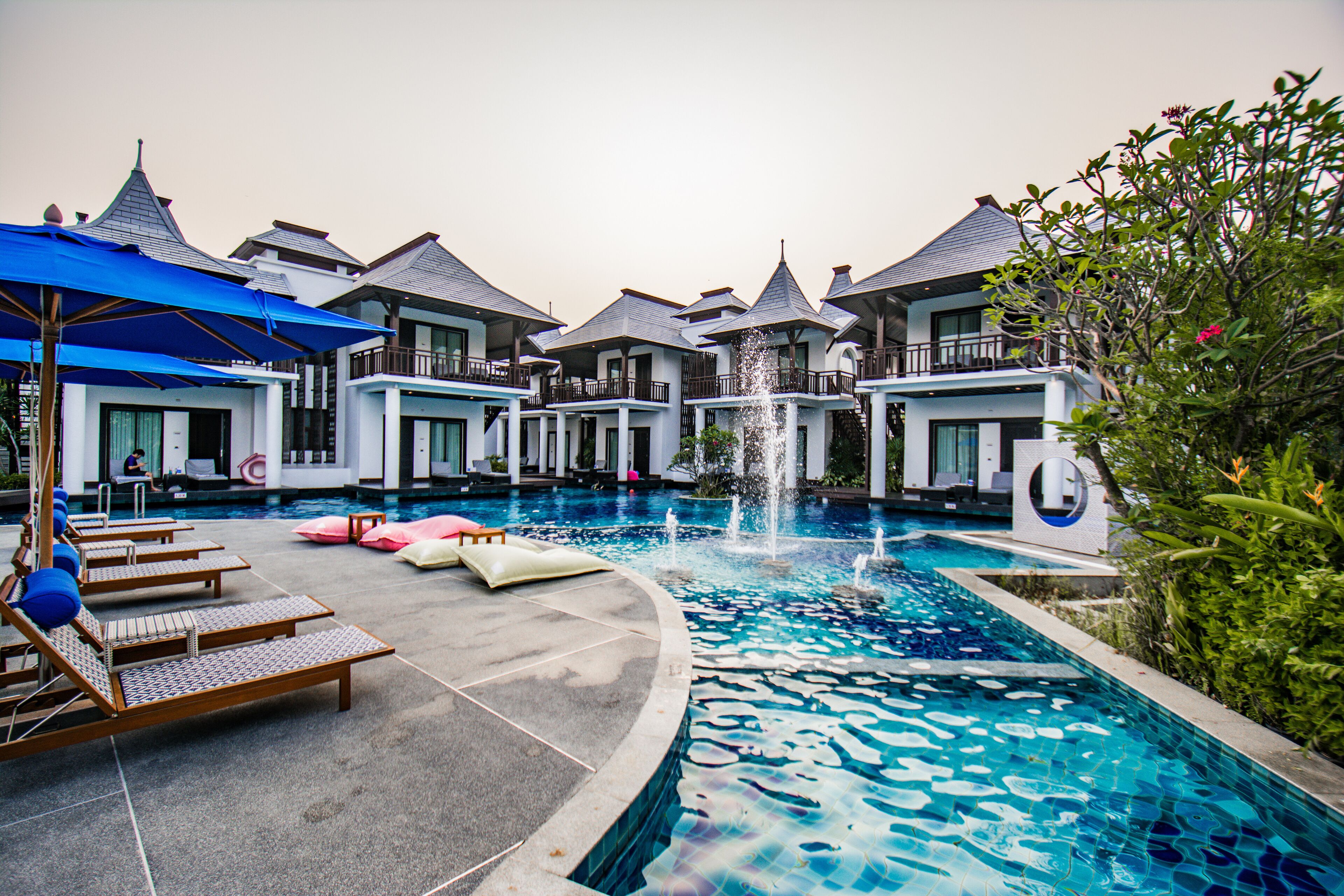 A pool area with lounge chairs, a fountain, and a building with multiple balconies.