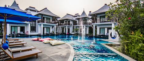 A pool area with lounge chairs, a fountain, and a building with multiple balconies.