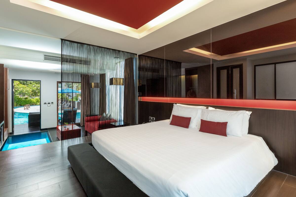 Quarto de hotel moderno com uma cama grande, vista para uma piscina e uma área de estar separada, também com vista para a piscina.