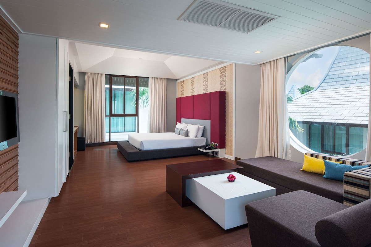 A modern hotel room with a large bed, a seating area with a coffee table, and a view of the outside.