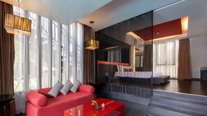 Habitación de hotel moderna con sofá rojo, una mesita de cristal, piscina y un ventanal con cortinas.
