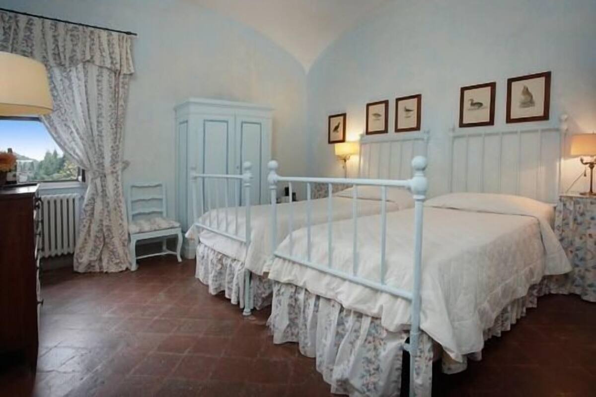 A bedroom with two beds, a white wardrobe, a radiator, and a window with curtains.