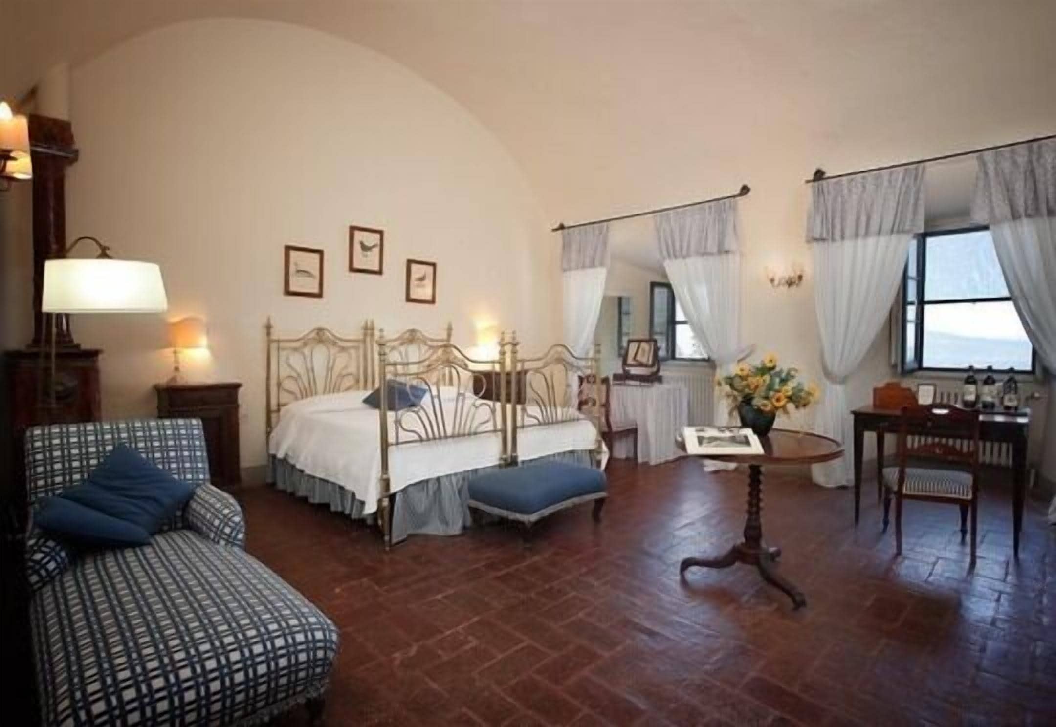 A bedroom with a four-poster bed, a small table with a vase, a chair, and a sofa.
