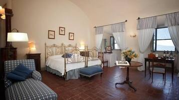 A bedroom with a four-poster bed, a small table with a vase, a chair, and a sofa.