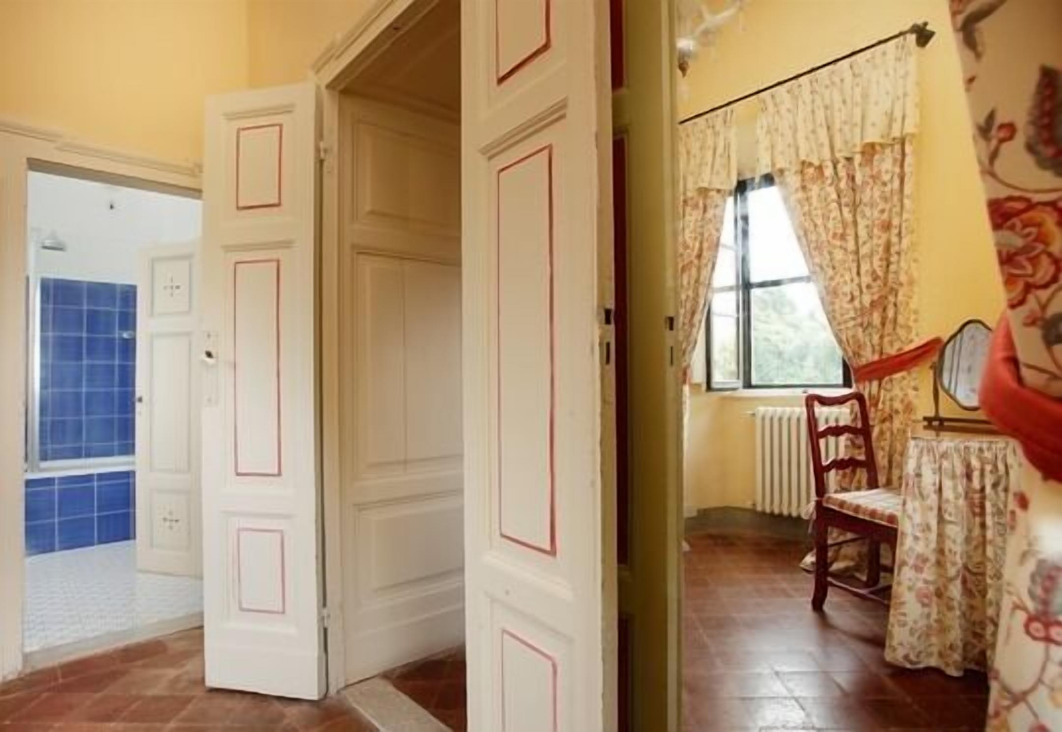 Una habitación con suelo de madera, una silla, una mesa y una ventana con cortinas.