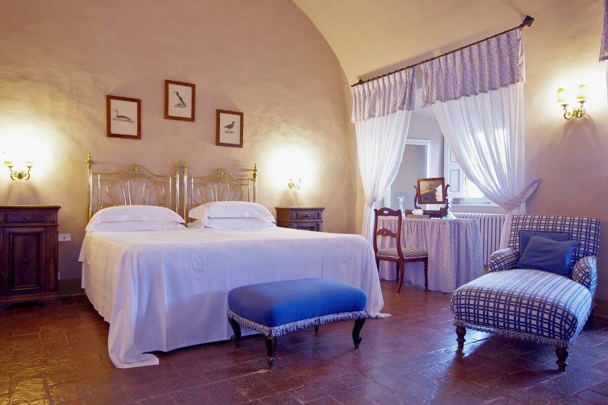 A bedroom with a bed, bench, chair, and a table with a chair.