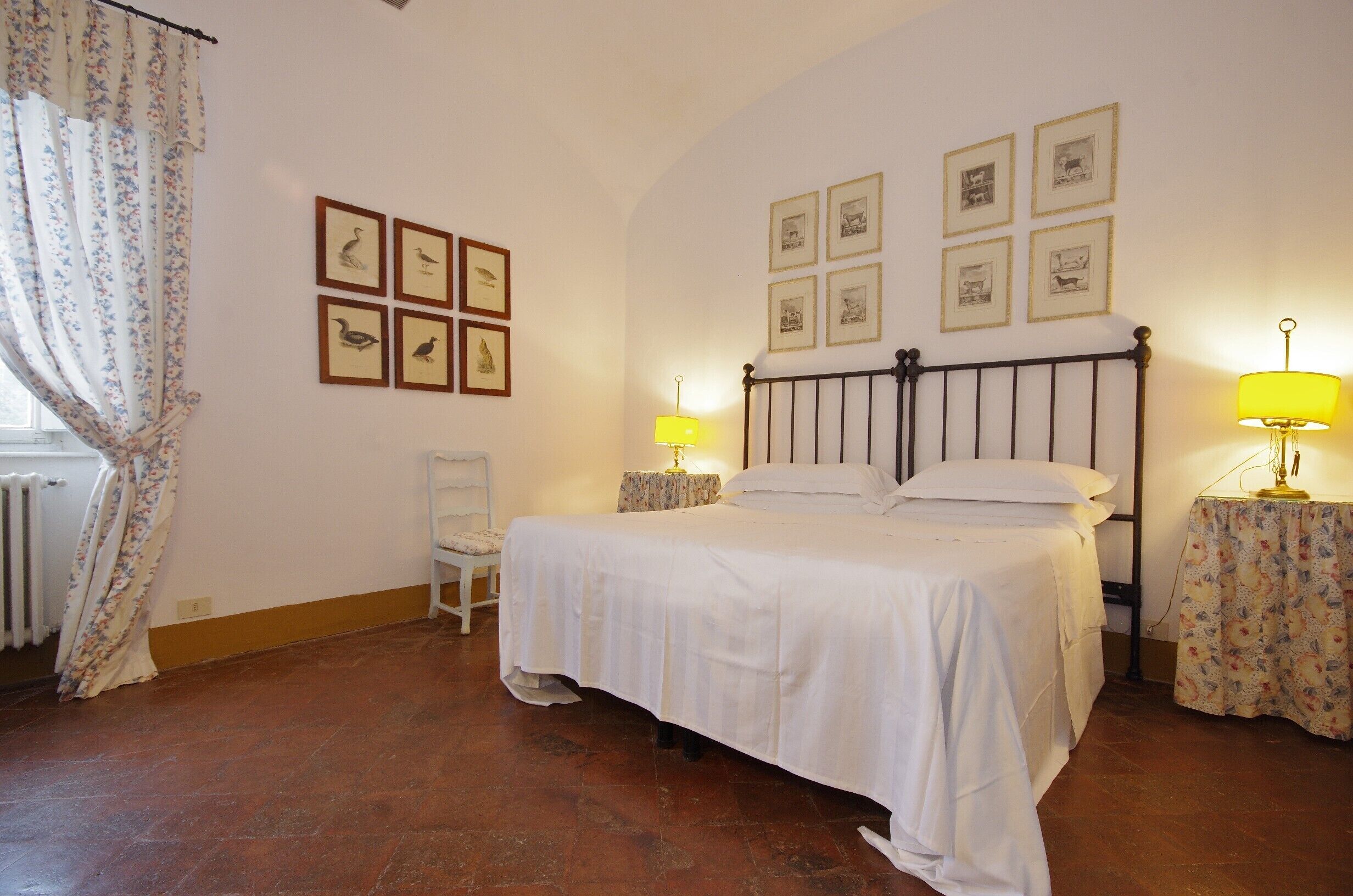 Une chambre à coucher avec un lit, deux tables de chevet avec des lampes, une chaise et des tableaux encadrés accrochés au mur.