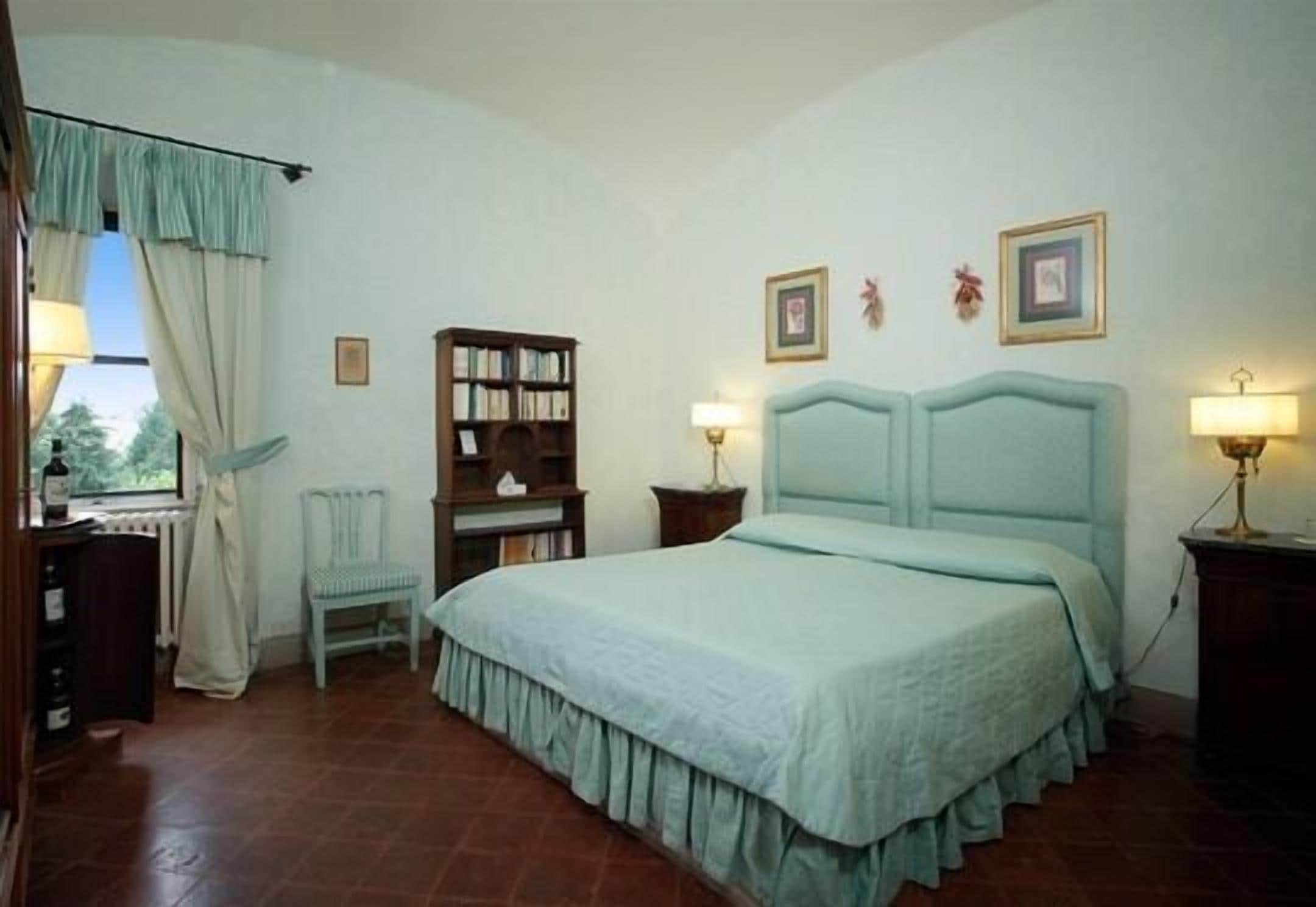 Une chambre à coucher avec un lit, une chaise, une bibliothèque et une fenêtre avec des rideaux.