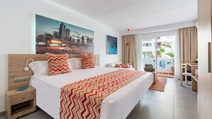 Habitación de hotel con una cama grande, una mesita de noche, un escritorio y vistas a la ciudad a través de la ventana.