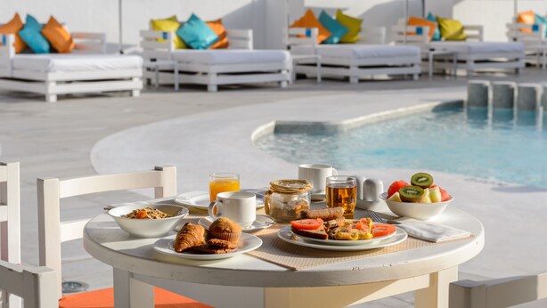 Desayuno junto a la piscina, con mesa, sillas y sillones de descanso.