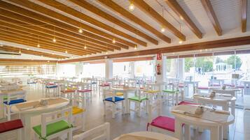 Spaziosa sala da pranzo con diversi tavoli e sedie, travi in legno a soffitto e ampie finestre che lasciano entrare la luce naturale.
