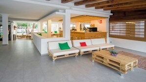 Un vestíbulo amplio con mostrador de recepción, un conjunto de sofás con cojines de colores y una mesa de centro de madera.