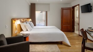 Una habitación de hotel con cama, mesita de noche, lámpara y televisor montado en la pared.