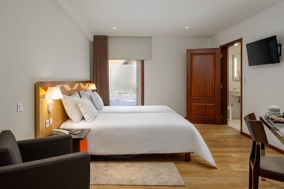 Ein Hotelzimmer mit Bett, Nachttisch, Lampe und einem an der Wand befestigten Fernseher.
