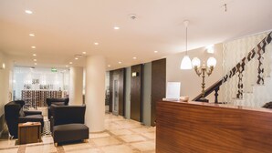 Zona de recepción de hotel con mostrador de madera, asientos negros y suelo estampado.