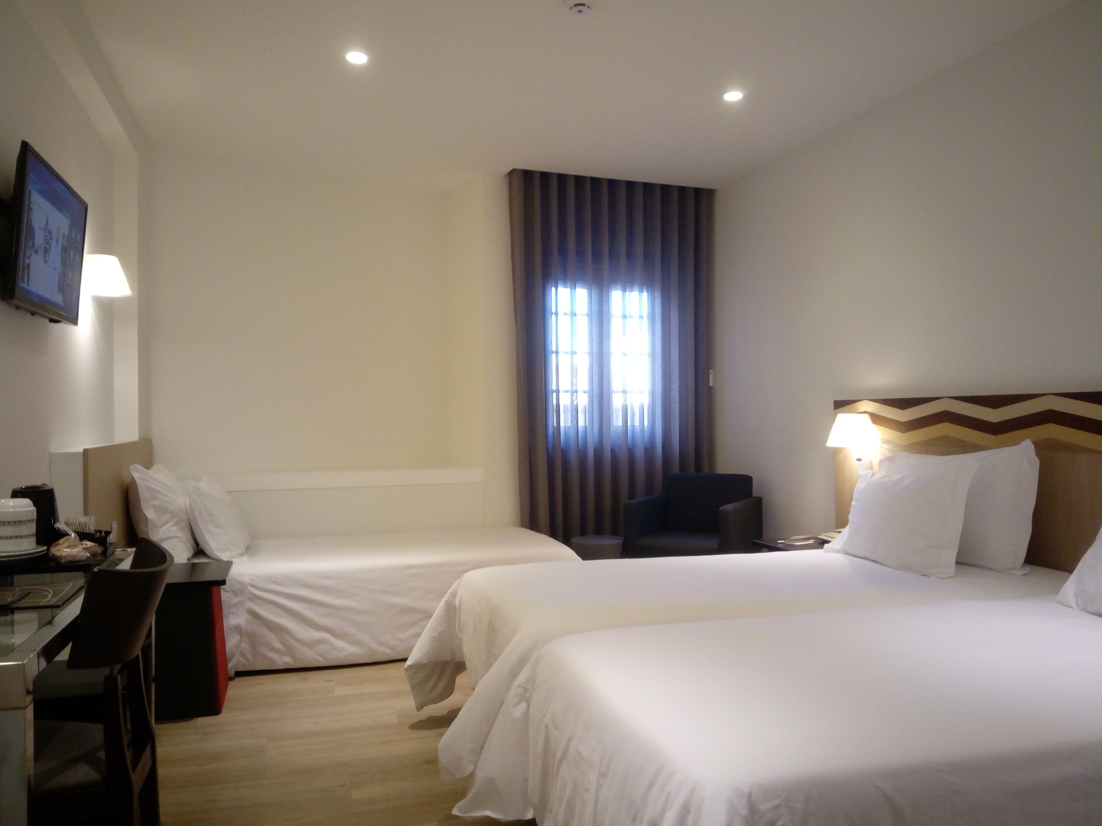 Una habitación de hotel con dos camas, un escritorio con silla, televisión y ventana con cortinas.