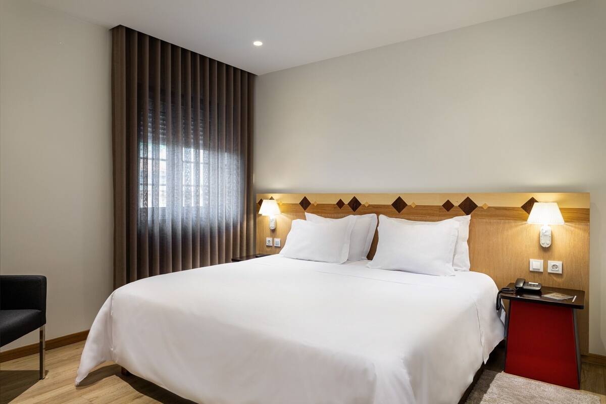 Ein Hotelzimmer mit einem großen Bett, einem Nachttisch mit Telefon und einem Sessel.