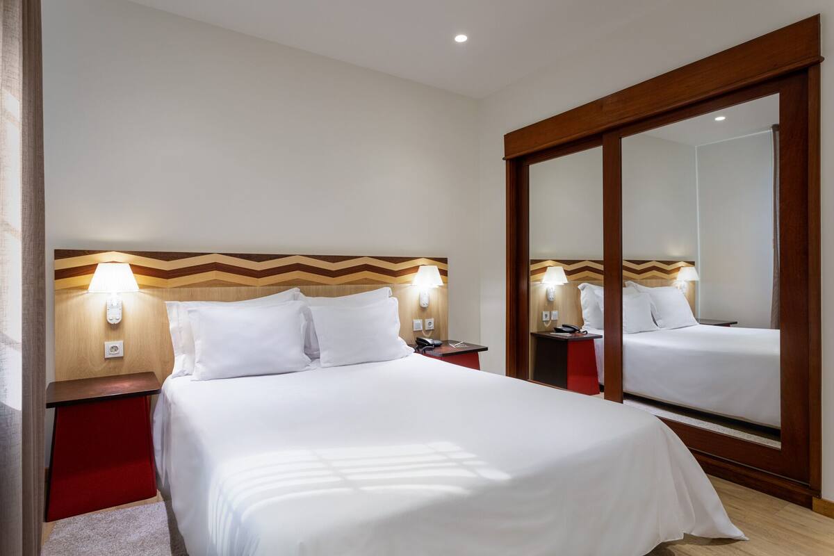 Ein Hotelzimmer mit einem großen Bett, einem Holzkopfbrett mit Zickzackmuster, Nachttischlampen, einem Nachttisch und einem großen Spiegel.