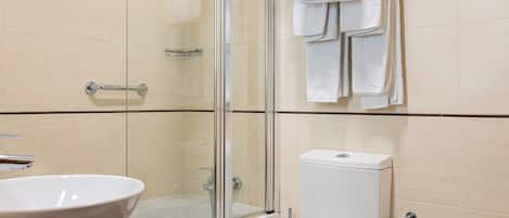 Un baño moderno con ducha envuelta en vidrio, lavamanos, inodoro, bidé y toallero con varias toallas.