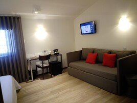 Una sala moderna con un sofá gris, dos cojines rojos, una mesita con una cafetera, una silla y un televisor de pantalla plana montado en la pared.