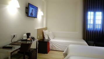 Een hotelkamer met een bureau, een bed, een aan de muur bevestigde televisie en een raam met gordijnen.