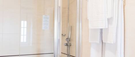 A glass-enclosed shower area with a towel rack holding multiple white towels.